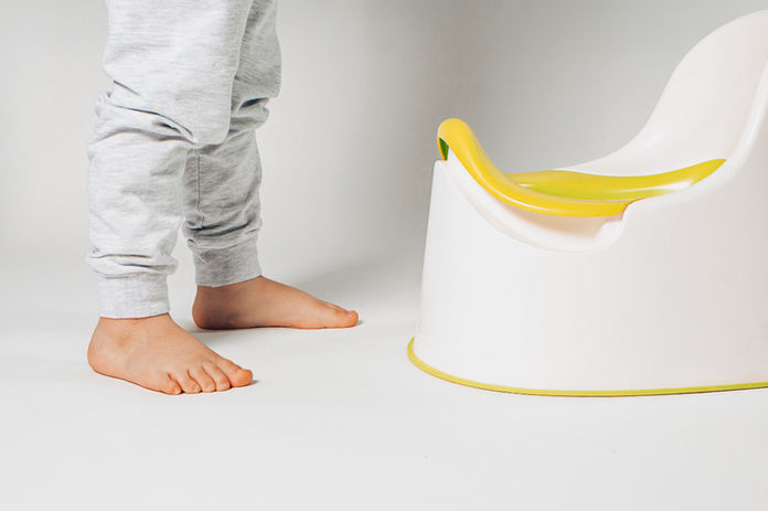 A toddler boy is standing over a training toilet. You can only see his legs and the potty, the rest of his body is not in the frame. 