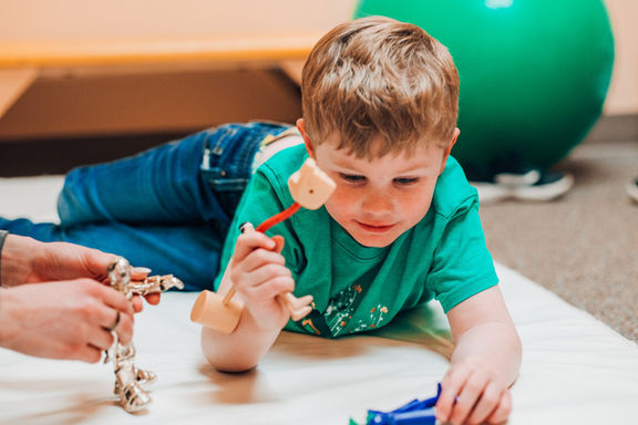 Boy lays on ground playing pretend with toys during a speech therapy session 