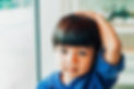 Young toddler boy looks at camera and has his hand on the top of his head.