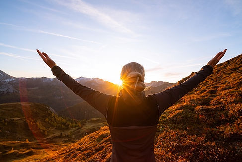 Personne les bras levés vers le ciel au sommet d'une montagne, au lever du soleil