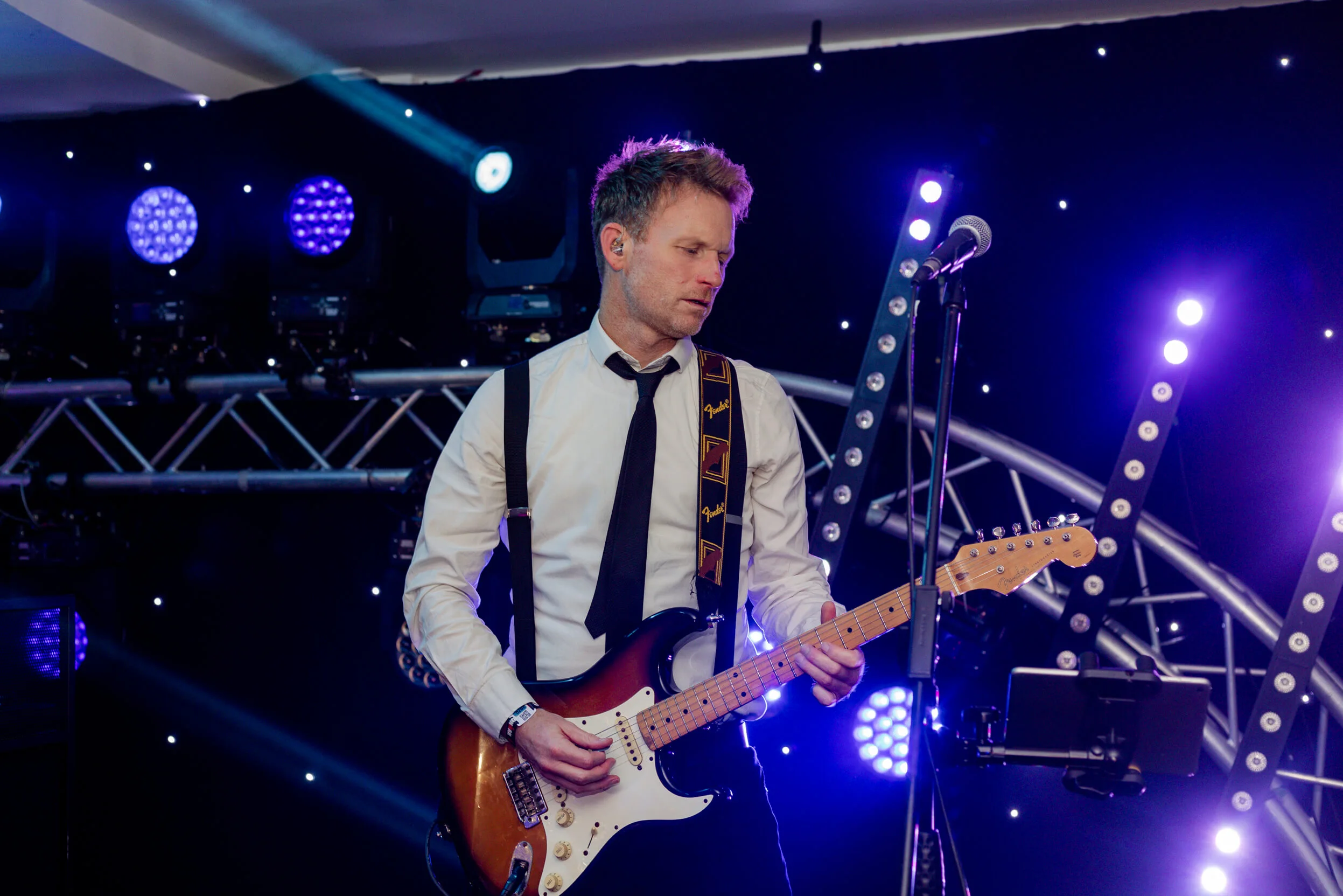 A musician playing an electric guitar on stage, with atmospheric purple lighting and a starry backdrop.