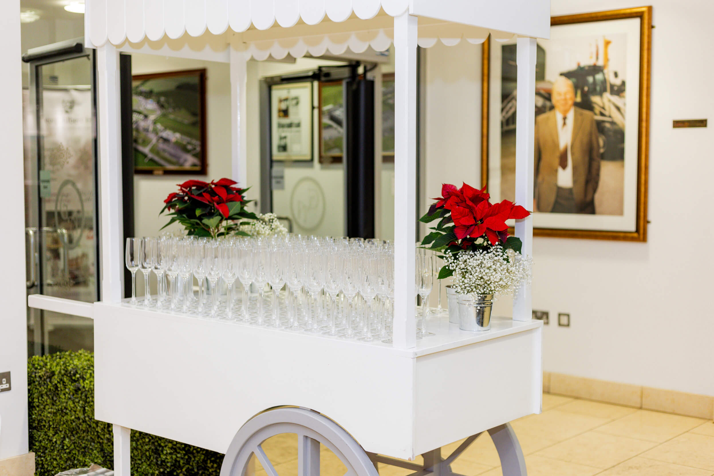 A white drinks cart decorated with poinsettias and glasses, ready to welcome guests at the Paris-themed event.