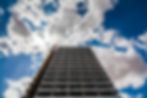 High-rise building with external cladding under a bright, partly cloudy sky, highlighting the importance of cladding fire risk assessments for safety compliance and fire prevention.