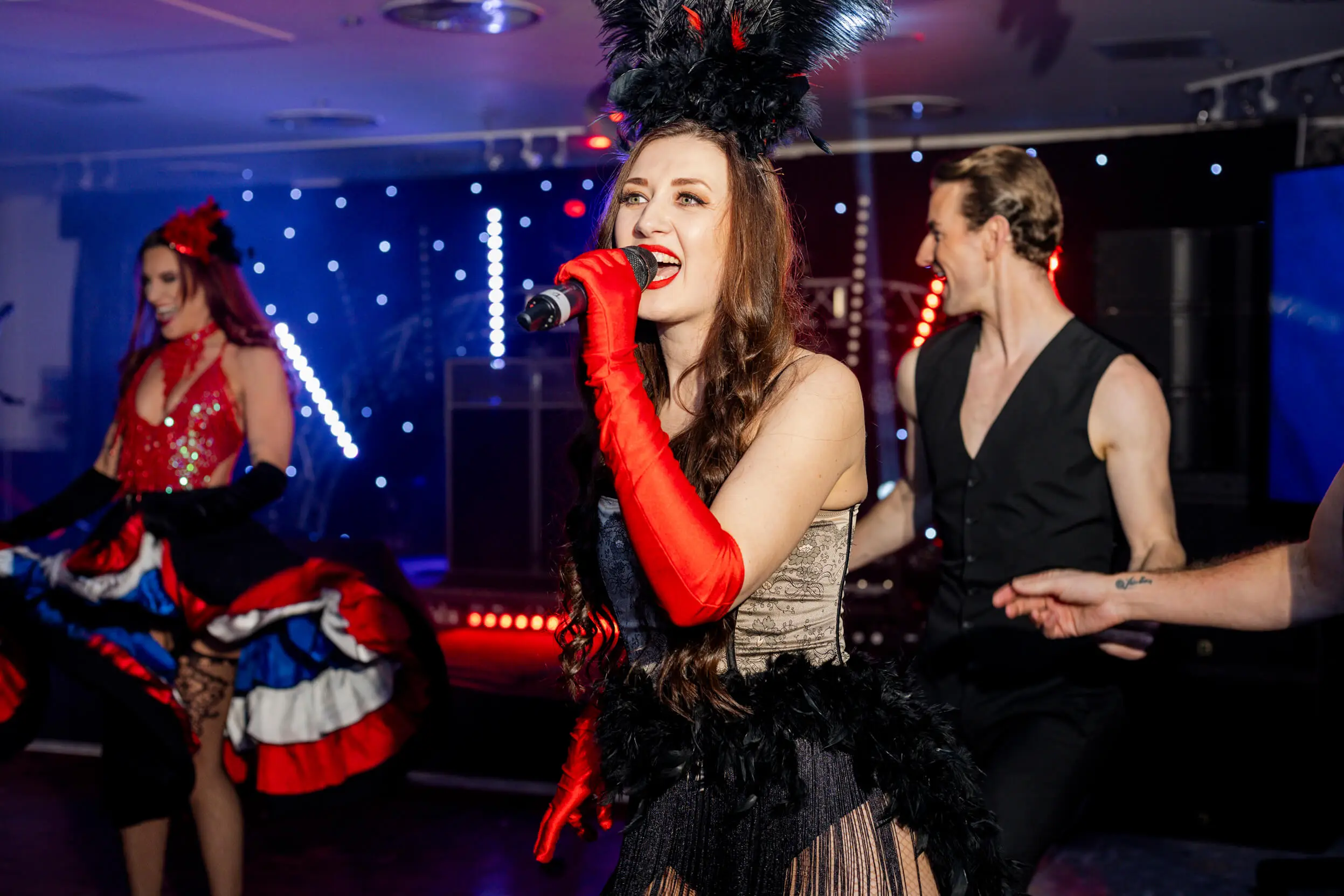 A performer singing with a vibrant costume, feathered headpiece, and red gloves, part of the Parisian-themed event.
