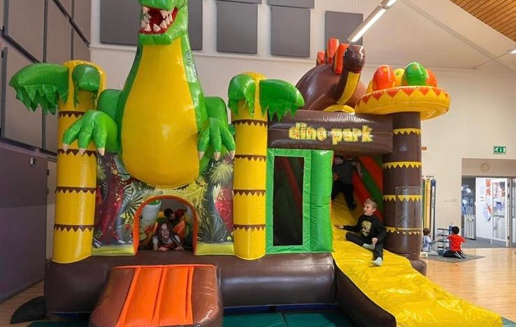 An indoor jungle-themed bouncy castle with a colourful dinosaur, creating a fun and adventurous play area.