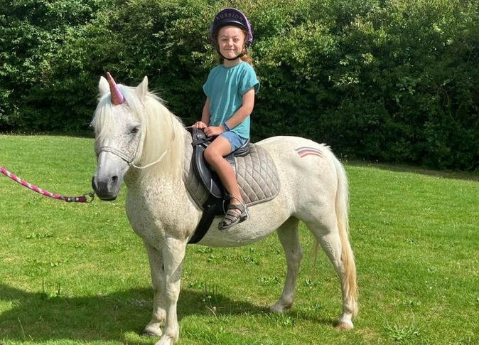 A girl happily posing on a unicorn outside during summer, enjoying a magical and playful moment.