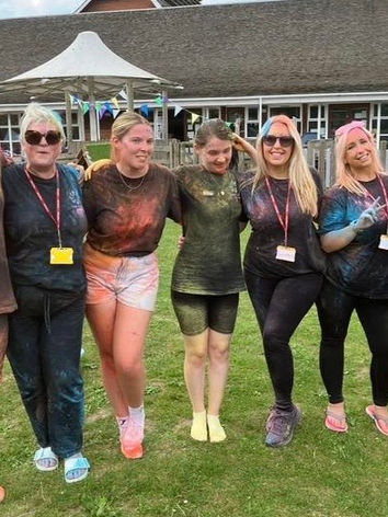 A staff team photo featuring everyone covered in vibrant powdered paint, smiling and laughing together after a fun and colourful activity.