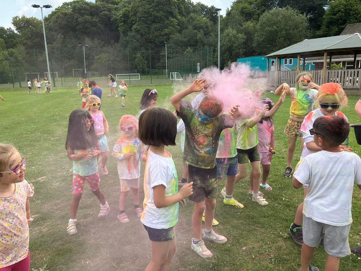 Children playing outside with powdered paint, laughing and tossing vibrant colours into the air, creating a fun and messy atmosphere.