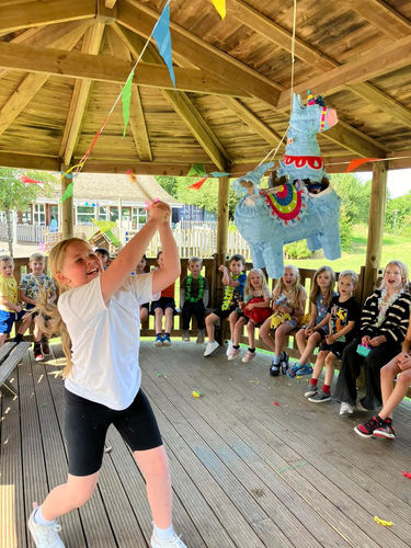 A girl eagerly swinging a stick to hit a colourful piñata, focused and excited as she tries to break it open while others watch in anticipation.