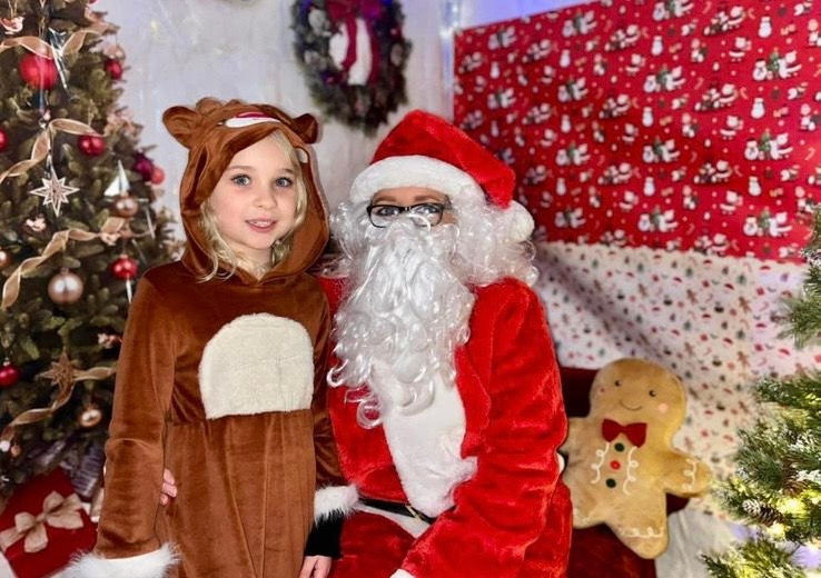 A cheerful girl smiling happily with Father Christmas beside a festive Christmas tree, enjoying a magical holiday moment.