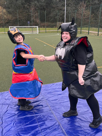 Two participants dressed in sumo wrestling suits, playfully engaging in a fun and friendly match outside, surrounded by an energetic and lively atmosphere.