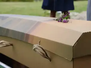 Close up of a cardboard casket with jute handles and flowers on top