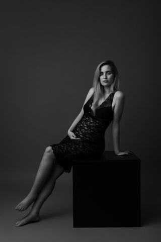 אישה הריונית יושבת על קובייה שחורה בסטודיו , עם שמלה תחרה, , מבט ישיר 