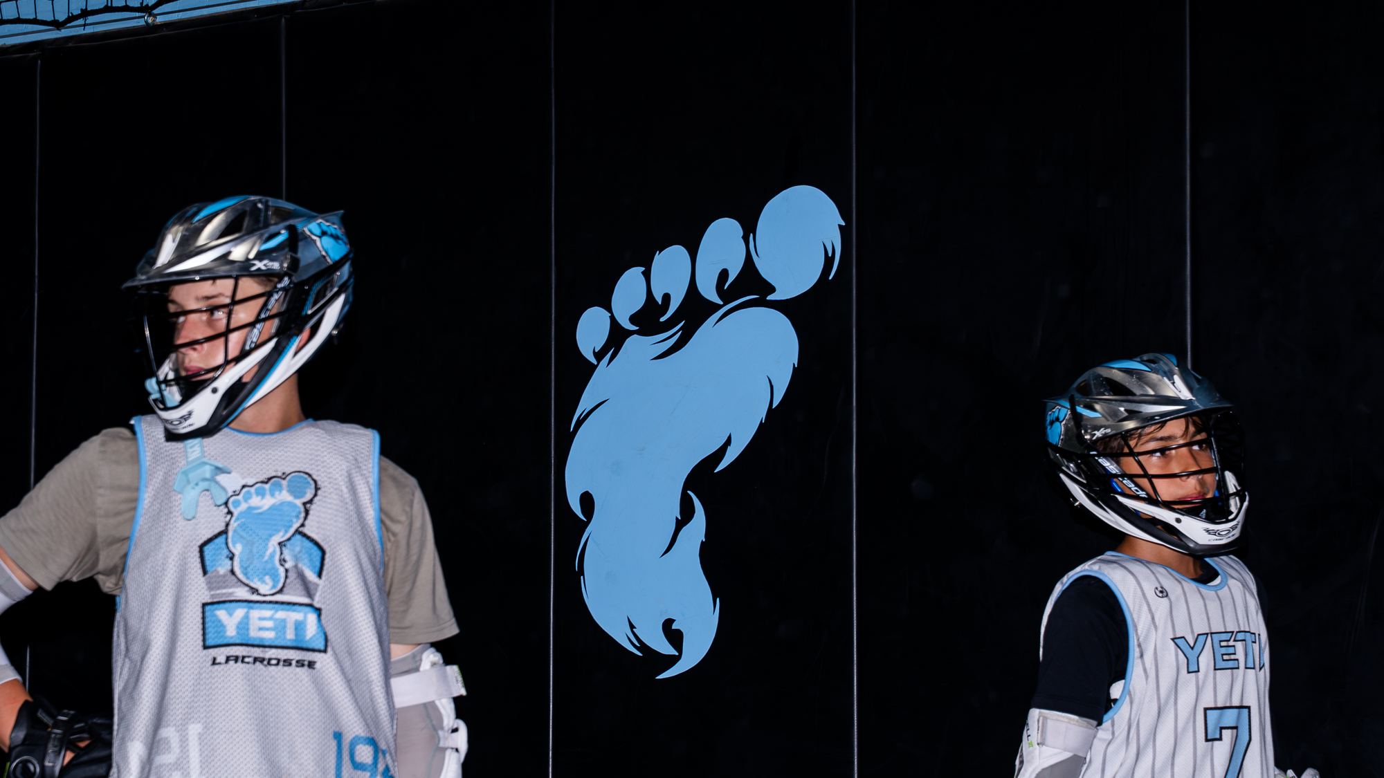 Two Yeti players in helmets in front of the Yeti footprint logo