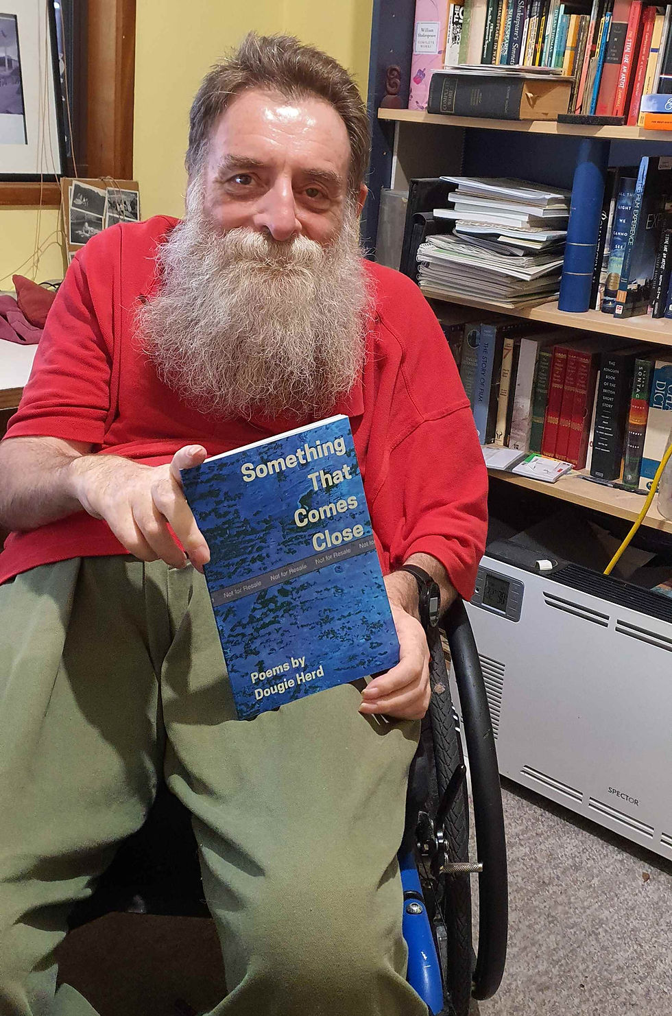Dougie sitting in his wheelchair presenting the cover of his book titled Something That Comes Close to the camera.