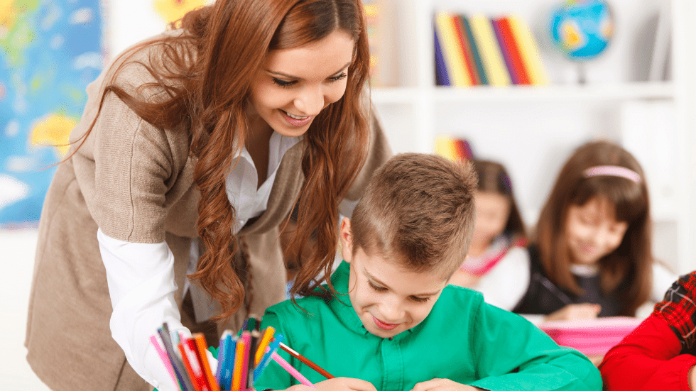 Smiling teacher helping a student write at a desk
