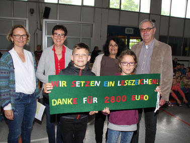 Kinder halten ein Plakat mit den Sätzen: Wir setzen ein Lesezeichen! Danke für 2800,- Euro