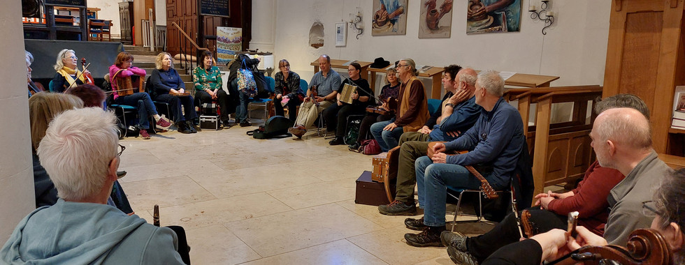 A group of 23 musicians sitting in a circle inside a church participating in a workshop