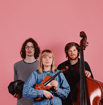 Grace Smith Trio holding their musical instruments standing in front of a pink wall