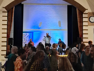 Three musicians (Dave Shepherd in the centre) are playing on stage with many dancers in the foreground.