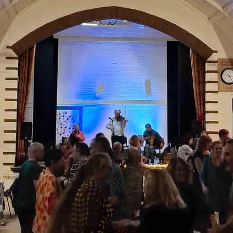 Three musicians (Dave Shepherd in the centre) are playing on stage with many dancers in the foreground.