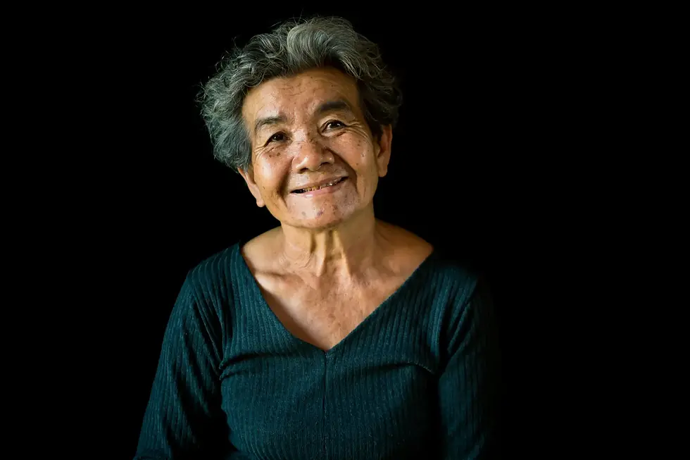 Smiling older woman in dark clothing against a plain background, representing independence and trustee retirement decision-making