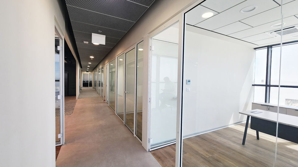 מסדרון מודרני במשרדי ברן, עם מחיצות זכוכית אקוסטיות מלאות וחדר ישיבות עם רצפת עץ אלון בסידור פישבון.