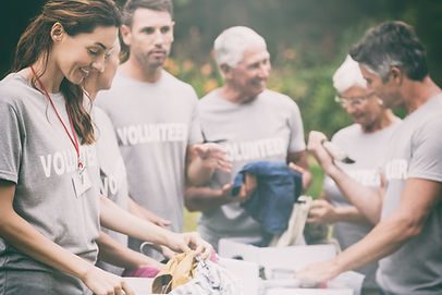 A group of people wearing grey shirts with the words volunteer on them. They look like they're planting or sorting something.