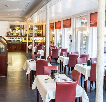 Moderner Speisesaal mit weißen Tischdecken, großen Fenstern und freundlicher Atmosphäre.