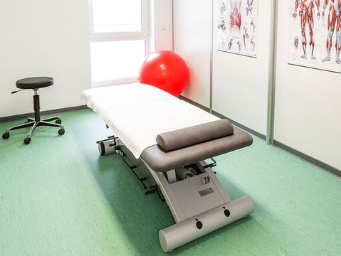 Behandlungsraum mit Untersuchungsliege und Gymnastikball in einem hellen, weißen Raum.