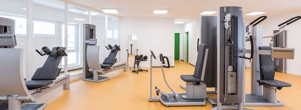 Fitnessraum mit Kraftgeräten, darunter Beinpresse und Brustpresse, in hellem Raum.