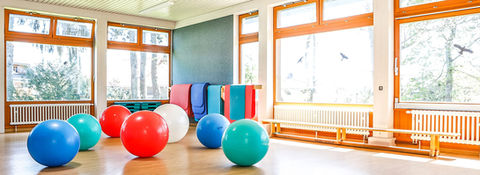 Bewegungsraum mit bunten Gymnastikbällen und großen Fenstern, viel Tageslicht.