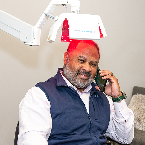 A man sitting under the HEC Clinical Hair Growth Laser device talking on his phone.