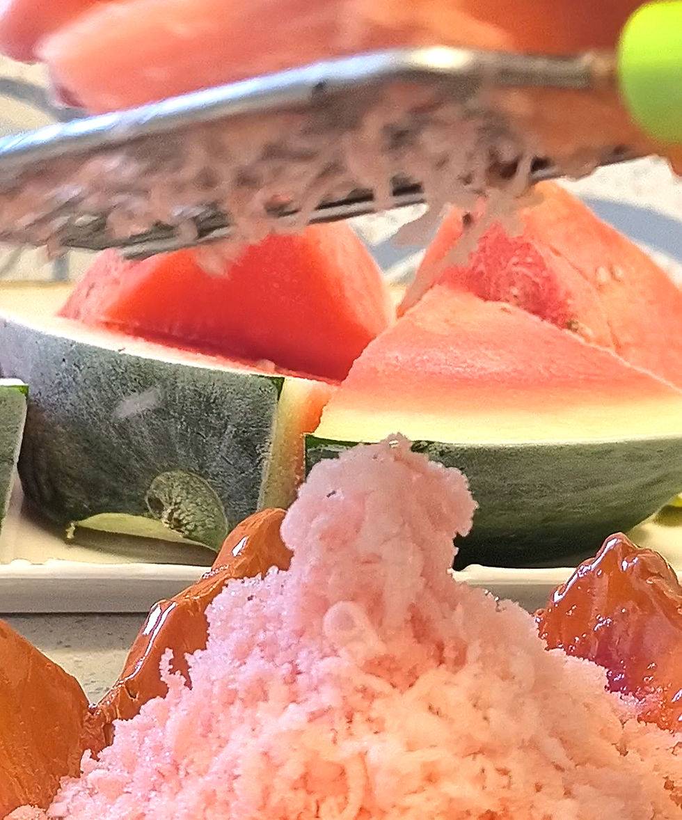 Grating watermelon over a bowl of pink shaved ice, with fresh watermelon slices in the background. Bright, summery colors.