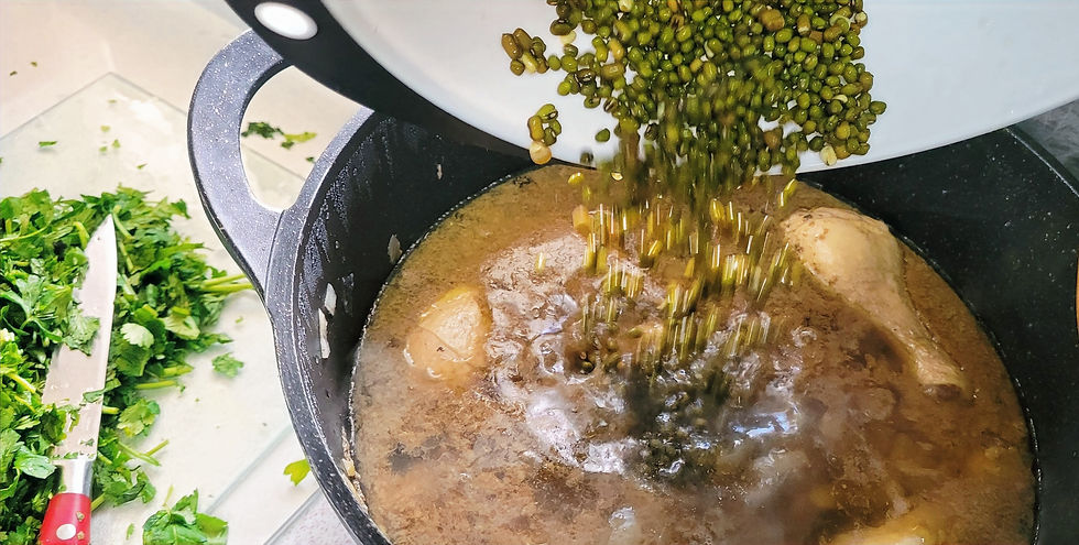 Green lentils being poured into a black pot with soup and chicken. Fresh cilantro and a knife are on the side. Warm, cooking scene.