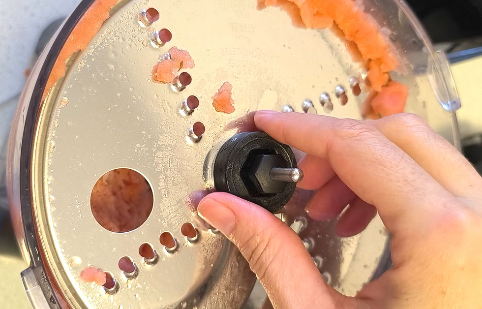 יד מסובבת דיסק פומפיה מעבד מזון עם פתחי עיגולים. שאריות כתומות על המכסה. רקע מטושטש.
