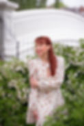 life coach Rosie is outside in a park with flowers behind, wearing a flowery red dress and laughing. She has long red hair