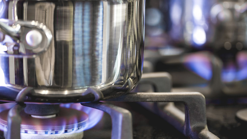 A shiny pot on a lit gas stove burner with blue flames. Reflective surface shows kitchen setting, creating a warm, cooking atmosphere.
