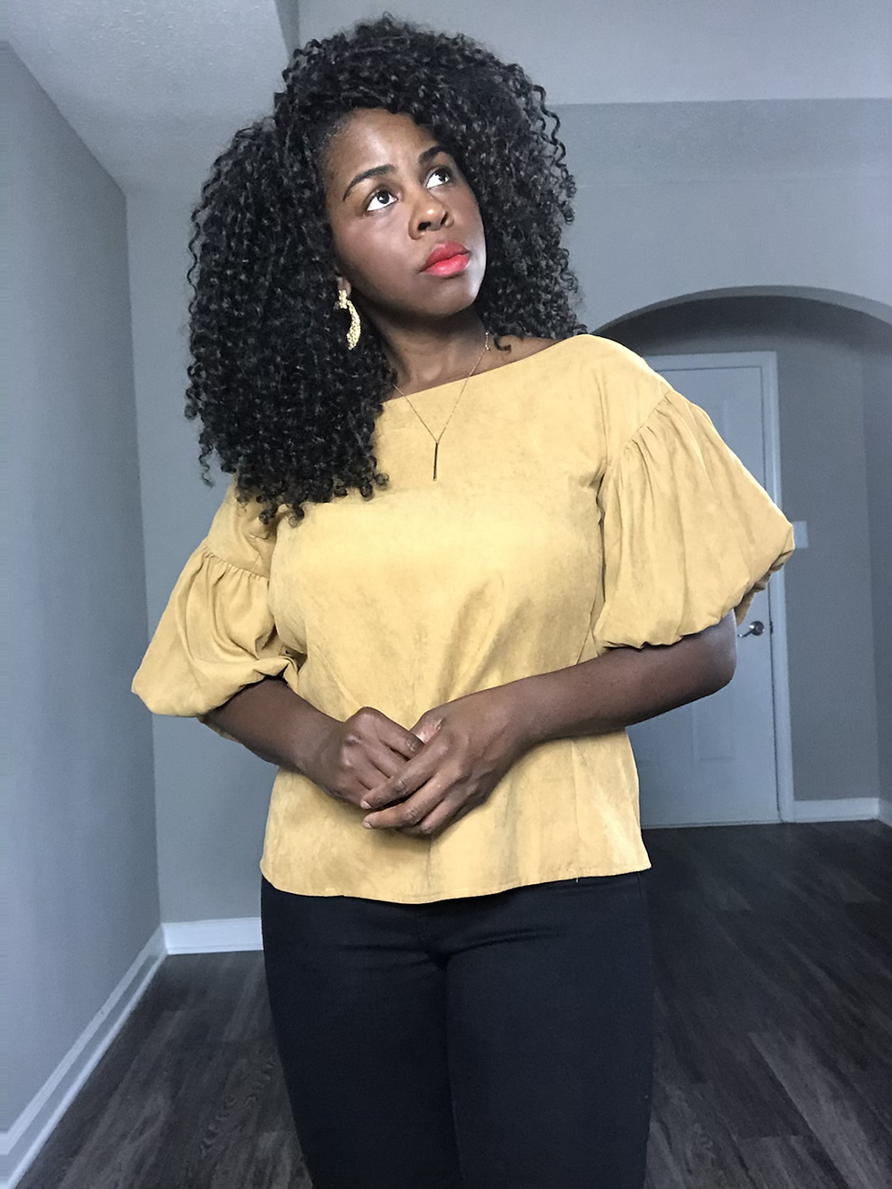 Thumbnail: Woman poses wearing a mustard blouse and black pants, looking thoughtful in a hallway.