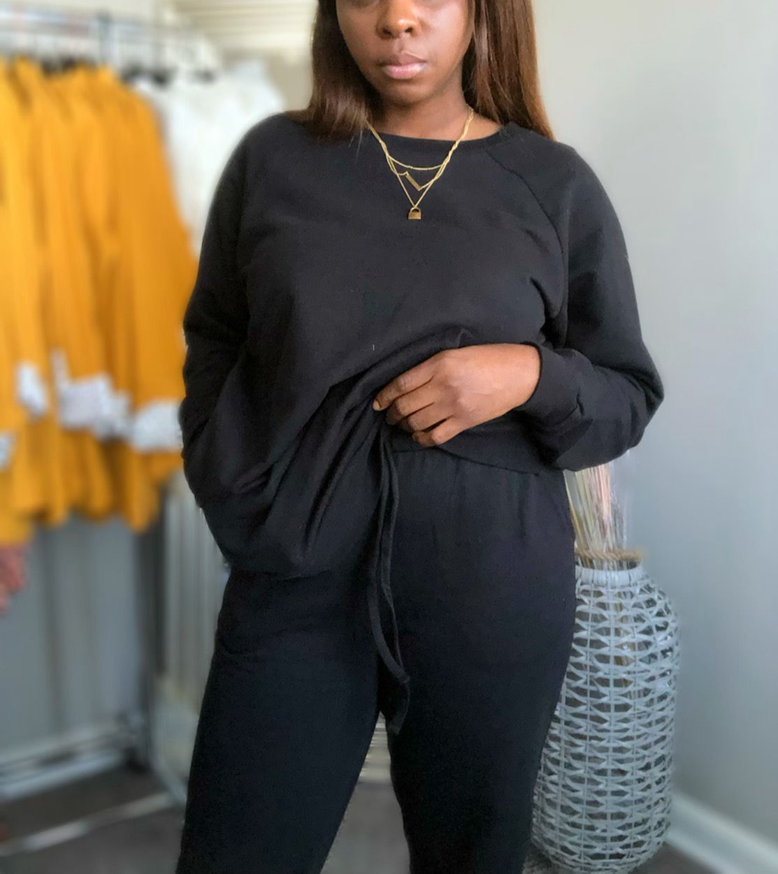 Woman in black sweatshirt and sweatpants, multiple layered necklaces, and background