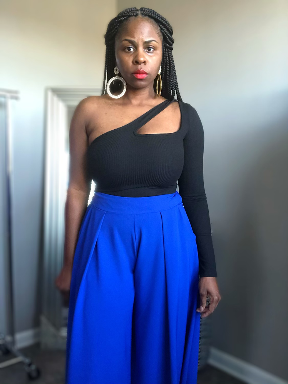 Thumbnail: Woman wearing one-shoulder black top paired with blue pants posing.