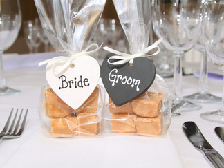 Two clear gift bags filled with fudge pieces, each tied with a ribbon and heart-shaped tags labelled “Bride” and “Groom”