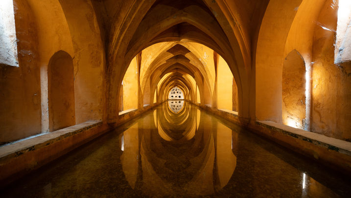 Vaulted arches reflected in the still water of the Baños de Doña María de Padilla, beneath the Real Alcázar of Sevilla.