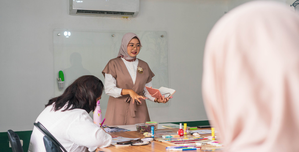 Kak Anug sedang memimpin sebuah Journaling Session di Pindrikan Markt 12, Collabox Creative Hub. Dalam sesi ini, peserta terlihat fokus mendengarkan penjelasan tentang teknik journaling untuk pengembangan diri (self-development). Ruangan penuh kehangatan kolaborasi, dengan alat tulis dan buku catatan berserakan di atas meja.