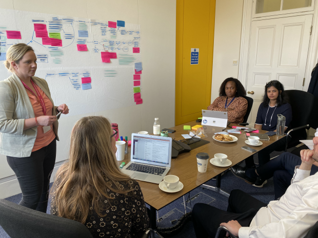 A wall of sticky notes with people around a table discussing it.