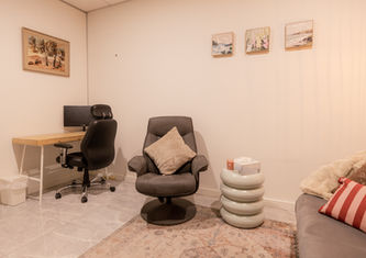 View from client’s perspective showing desk, chair, therapist couch, side table with tissue box and candle, and wall art in Consultation Room 5 Upstairs