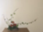 A minimalist ikebana arrangement with red and orange flowers, green leaves on long branches, set on