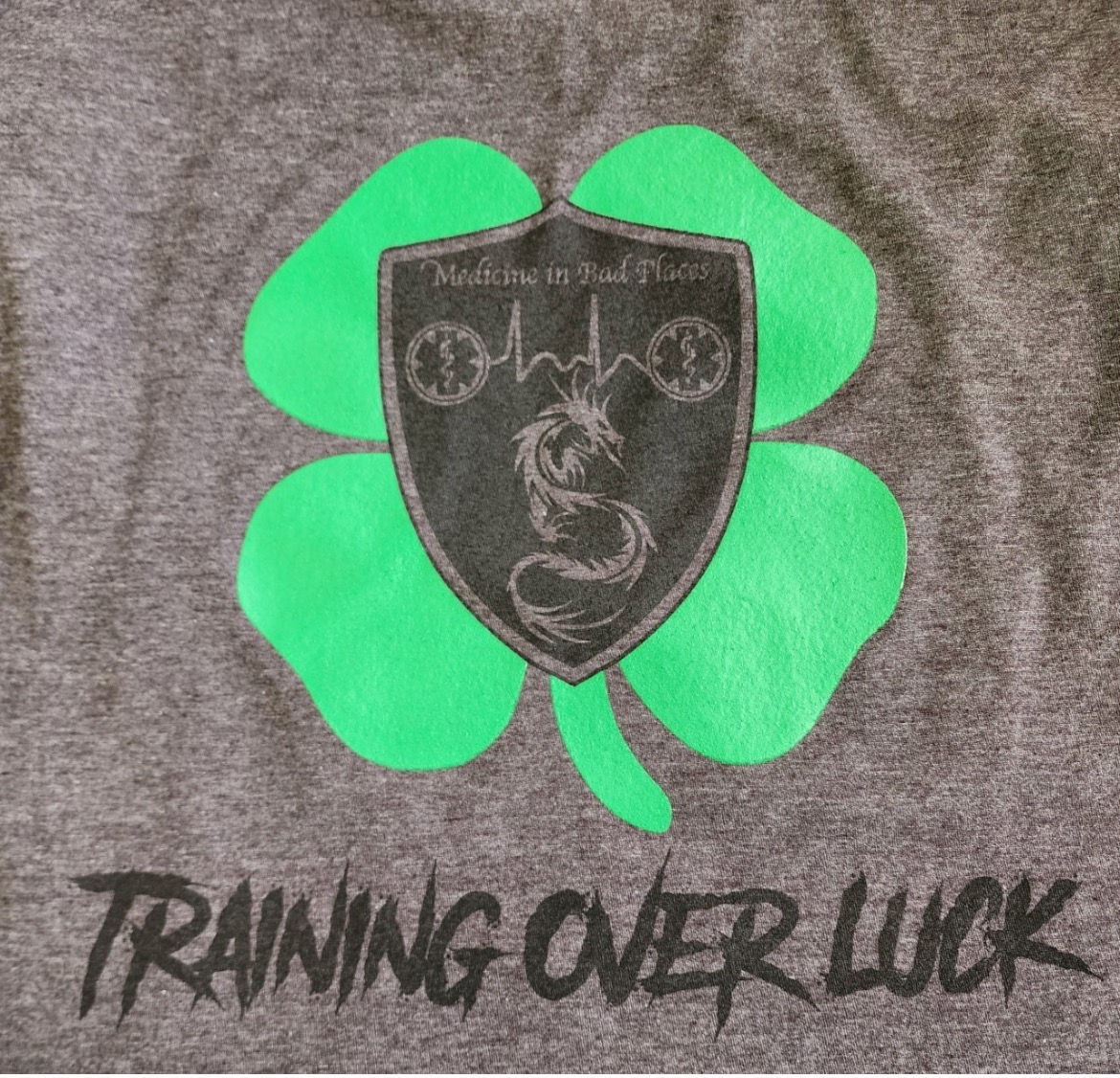 Shamrock back design with MIBP logo in center words under design say training over luck