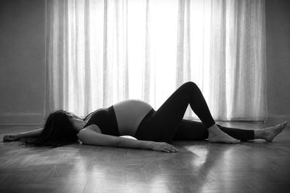 Femme enceinte allongée sur le parquet devant une fenêtre lors d’une séance boudoir grossesse à Amiens.