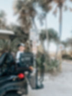 Thumbnail: Black soft cooler mounted on the rear seat armrest of a golf cart using the Cooler Caddie bracket, shown near a beach.